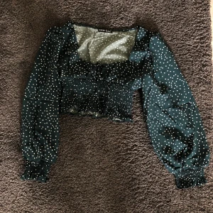 Blus i grönt med vita prickar - Gullig kall mörk grön blus med vita prickar och snörning framtill. Bra kvalite och endast testad en gång. Är strl S men känns mer som en XS 