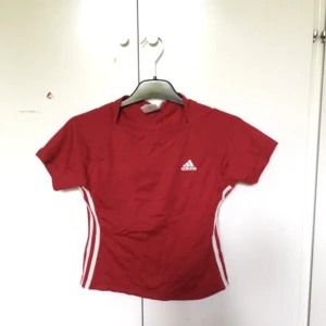  - Röd adidas t-shirt. Liten logga på bröstet och 3 streck på var sida. 