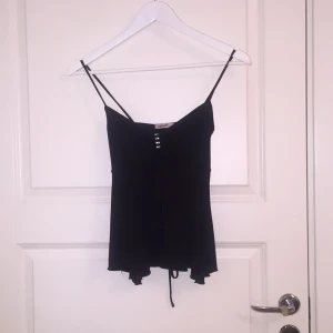  - Svart linne, längre bak över rumpan, med en detalj mellan bysten