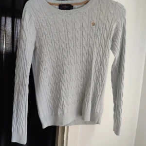 MORRIS KABELSTICKAD TRÖJA XS - Ljusblå tröja från Morris i storlek xs. Sparsamt använd men har ett litet hål i armhålan som nog är lätt att laga. Köparen står för frakten!