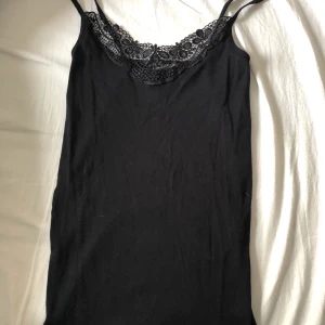Linne, S - Svart tajt linne med lite spets vid toppen av bröstet. 