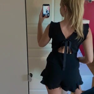 Playsuit med volanger - Säljer en playsuit som har både volanger vid benen och vid axlarna, den har två fickor framtill och är lite öppen i ryggen med en rosett som knyte (samt dragkedja vid sidan) Den är endast använda en gång! Storlek: M