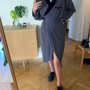 Vintage omlottklänning  - Vintage omlottklänning med krage i sammet med broderad kant och med sidoknäppning. kvalitén och skicket är väldigt fint, känns i princip oanvänd. Finns även axelvaddar till som kan sättas på. Hämtas i Malmö eller skickas med post. 