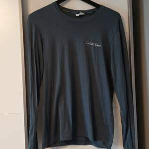 En blågrå långärmad T-shirt från Calvin Klein. Nästan som nyskick. Se tredje bild för skavank. Frakt ingår.