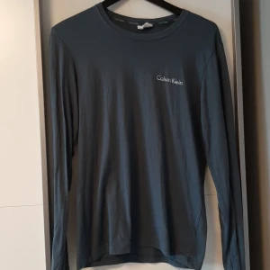 Långärmad t-shirt Calvin Klein - En blågrå långärmad T-shirt från Calvin Klein. Nästan som nyskick. Se tredje bild för skavank. Frakt ingår.