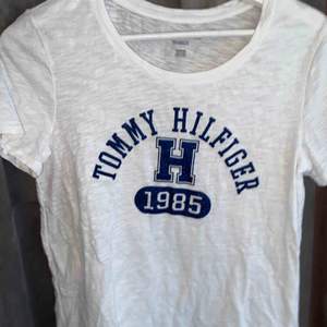 Vit Tommy Hilfiger t-shirt med blått tryck på bröstet. Denna är aldrig använd och köpt i höstas. Superfin och bra till sommaren.
