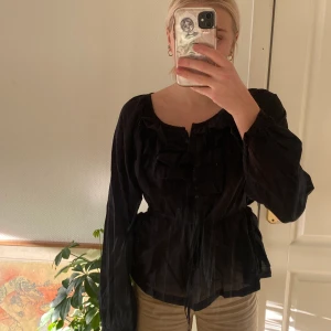 Svart blus med volanger och knytning - Svart tunn och skön blus som går att ha till vad som helst! Vet inte var den kommer ifrån. Ungefär storlek S/M.