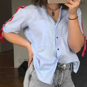  - En skjorta men röda detaljer på armarna, inga knappar hela vägen upp. Storlek i xs men den är lite större i sin storlek. Inte använts så mycket.  Frakt 65kr