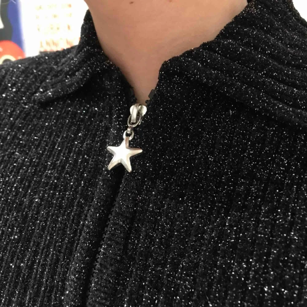 Superfin svart/silvrig glittrig tröja! Jättefin liten detalj på dragkedjan i form av en stjärna. Passar storlek XS/S beroende på hur du vill att den ska sitta. Skicket är mycket fint och den är knappt använd!. Tröjor & Koftor.