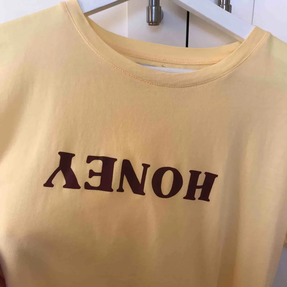 Härligt gul tröja med brunt/vinrött tryck ”HONEY” spegelvänt och uppochner. STRL S. I mycket fint skick! Skriv för fler bilder :) Frakt tillkommer, annars kan vi mötas upp i Kalmar.. T-shirts.