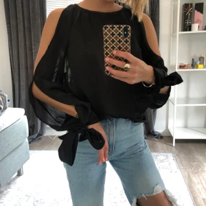 Svart blus från Ginatricot - En otroligt fin blus med lite öppna armar och knyte längst ner på armarna. 