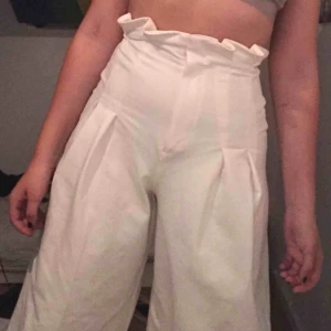  - Fint vitt material, straight leg med lite utåt stående, volang längst upp och figursydda, priset kan ändras