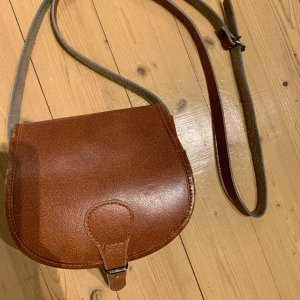 Handväska i äkta skinn.  - Brun skinnväska med två fack dör ett är lagom till ett par solglasögon. Bra kvalitet och skick. Säljer då den inte används. 