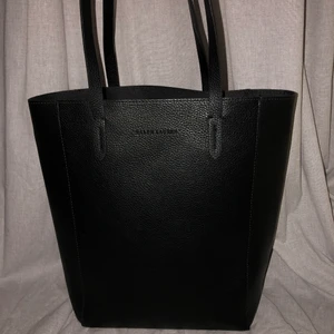 Helt oanvänd Ralph Lauren väska - En ny väska från Ralph Lauren i konstläder. Det är ingen dragkedja men det finns ett längre axelband att sätta på. Det finns heller inga fack i väskan. Mått: 35x29cm. Kan skicka fler bilder vid intresse 