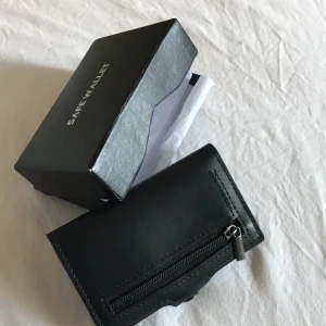 Helt ny safe Wallet i svart fakeskinn - Snygg och stilren, tjuvsäker plånbok. Aldrig använd, i orginalkartong. Fake svart läder, perfekt storlek, 5 kort. Perfekt som present till vem som. Kan samfrakta och säljer mycket mellan 10-100kr. Frakt - 44kr. (Utan kort & kartong - 22kr) 💗⚡️