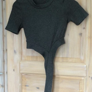 Topp - En grå t-shirt med band som man fäster på ryggen. Är köpt på chiquell för flera år sedan. Använd men i bra skick. Står ingen storlek i plagget men tror den är i S. 