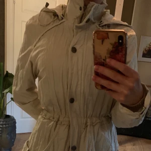 Vårjacka / höstjacka - En beige jacka från Rosebud i storlek S. Dragsko i midja. Stor luva och fickor i fram. Dragkedja och knappar.