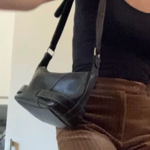 Svart väska - Svart läderväska i 90-tals stil med justerbar axelräm. Köpt här på plick men kommer inte till användning tyvärr. Lite slitningar på utsidan men annars i gott skick. 