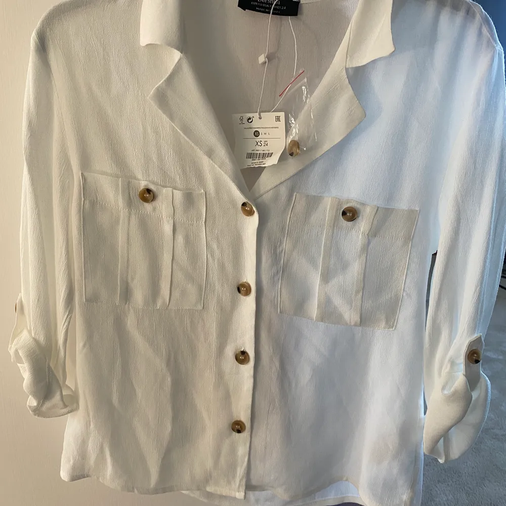 Superfin vit skjorta som har fina ”bruna” knappar på. Aldrig använd då prislappen är kvar och du får med en extra knapp. Armarna kan man både ha som det är på bilden eller knäppa upp och ha som en vanlig ärm. (priset är diskutebart). Skjortor.