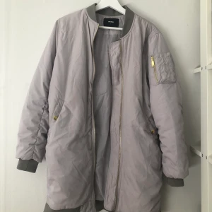 Lång bomberjacka från Bikbok - Lång bomberjacka från Bikbok. Ljusgrå/silver aktig, storlek S. Knappt använd, nyskick. 200kr 