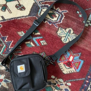Carhartt-väska - En svart Carhartt WIP axelremsväska. ”ESSENTIALS BAG SMALL UNISEX” Nypris: 499kr. Använt den en del, men det är inget som märks. Säljer pga har en liknande väska <3 Köparen betalar frakt!