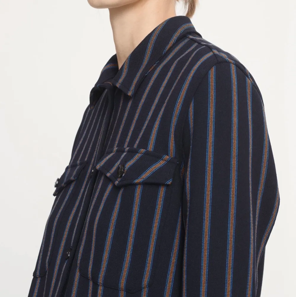 Säljer en mörkblå skjorta med brun & ljusblåa ränder på. Två fickor på framsidan. Knappt använd. Ordinarie pris 1999 kr . Skjortor.