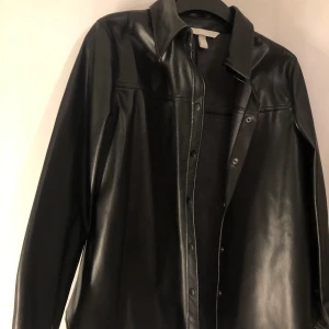 Svart skinn skjorta  - En svart oanvänd skinnskjorta, köpt från h&m. Helt ny. Går jätte bra att även ha som jacka. Storlek 38, men passar lika bra för er som har 34-36