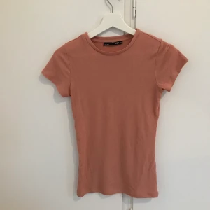 Rosa T-shirt  - Nästan gammalrosa lite ribbad T-shirt. Från lager 157 i mycket bra kvalitet. Frakt tillkommer som köparen står för. Priset går att diskutera. Vid frågor så är det bara att höra av sig.