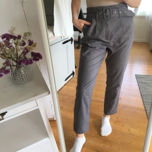 NAKD kostymbyxor - Gråa kostymbyxor med bälte från NAKD. Frakt tillkommer på 60kr och betalas via Swish. 