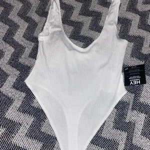 Body vit linne - Ribbad vit body linne med djup urringning fram och bak. Storleken är mer som S/M