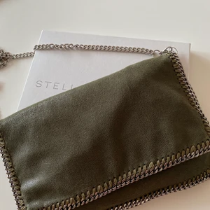 Stella McCartney väska - En mörkgrön Stella McCartney väska, kan bäras som både clutch och vanlig väska då kedjan går att ta av och på. Inköpt för 3000kr på vestiaire collective för ca 6 månader sedan. Inga märkbara slitningar på väskan. Rymmer mycket då den har många olika fack.