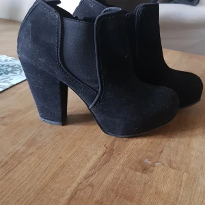 Stövlett Tiamo - Sparsamt använd stövlett i svart mocka med platå fram och 10 cm kraftig klack. Dragkedja på insidan och infälld resår på utsidan. Sköna att gå i.