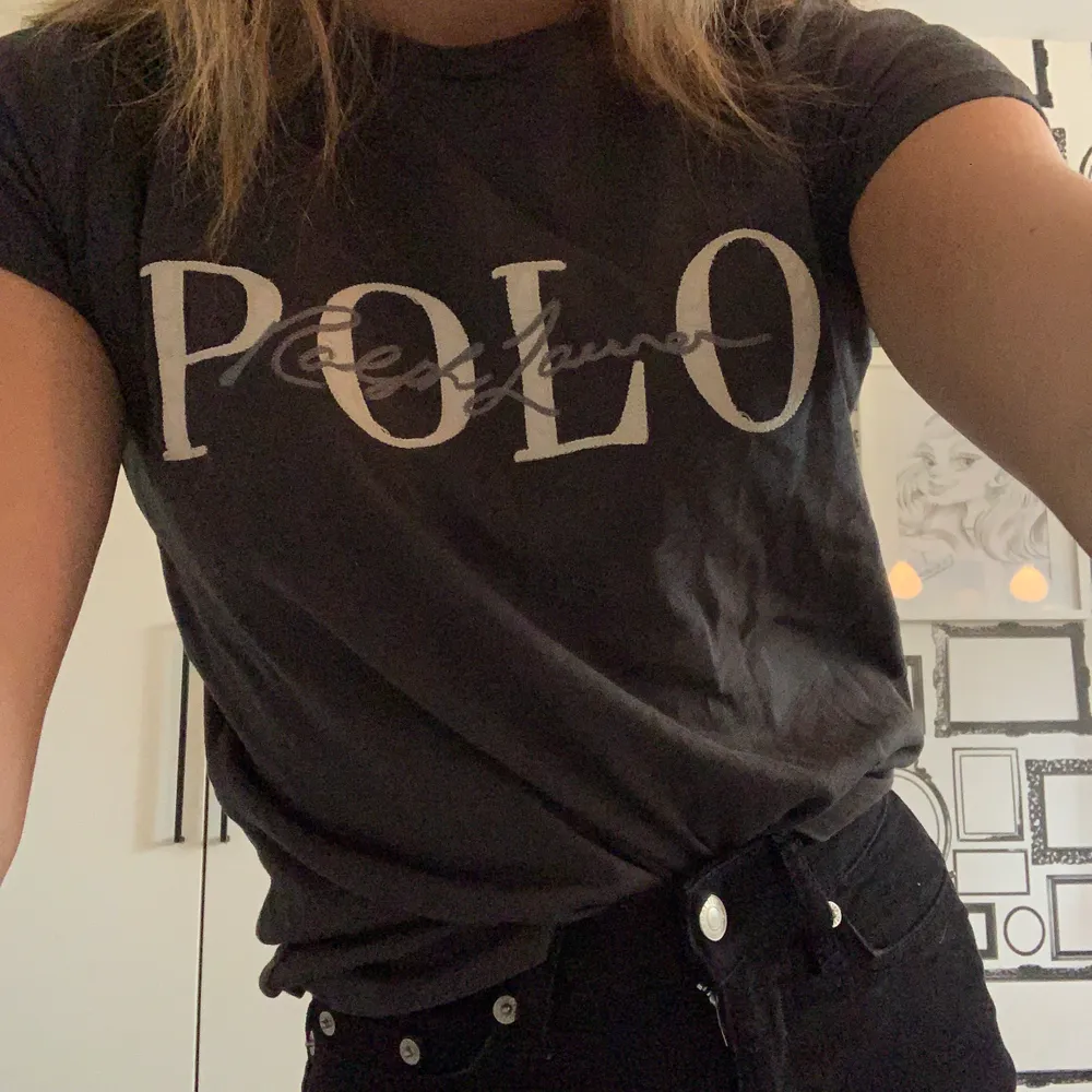 En svart/grå t-shirt med en vit och grå text där det står ”Polo Ralph Lauren” från Ralph Lauren, knappt använd!! Storlek XS. T-shirts.