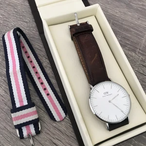 Daniel Wellington klocka - en dam Daniel Wellington klocka 36 mm i silver. i priset ingår klockan med både det bruna läderbandet och det randiga tygbandet samt spårbar frakt! allt med silverdetaljer. saknar kvitto men kan garantera äkthet. 