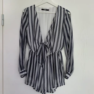 Randig jumpsuit - Blå- och vitrandig jumpsuit i storlek XS som knyts framtill från Bik Bok. Den är långärmad med öppning över armarna och är i shorts modell. Pris: 100kr+frakt (44kr).