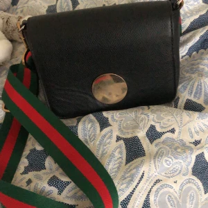 Axelremsväska svart  - Säljer min axelremsväska med ett sjukt snyggt band, går att byta ut om så önskas 🥰. Frakt tillkommer på 70 kr om man vill ha den fraktad, annars möts jag upp. 