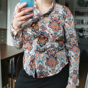 Paisley skjorta - Skjorta med paisley-mönster, strl 36. Byst 92 cm, längd ca 56 cm från axeln (rundad nederkant). Jättefint skick! Köparen står för porto 63 kr (spårbart) 
