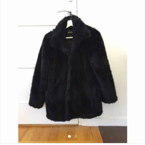  - Svart fuskpälskappa med liten krage och en stängning med hakar. Två rymliga fickor. Varm och supermysig. Och SNYGG! Går nedanför rumpan på mig som är 164cm. 