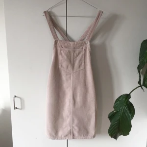  - Beige hängselklänning i manchester-tyg från Topshop. Aldrig använd. Materialet är 100% bomull. Frakt ingår i priset. Fin nu till sommaren! Obs den är inte fläckig i färgen, bara svår att fånga på bild pga materialet.