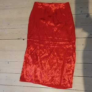 Röd knälång kjol i satin - Kjol köpt från hm för några år sen som aldirg kommit till användning. Sitter fint på kroppen och över rumpan. Behöver strykas som ni kan se och den har en slit vid ena benet. 😊 Ni får gärna skriva ifall ni har frågor eller vill se fler bilder av plagget. ❤