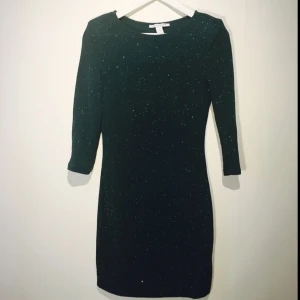  - Mörkgrön, glittrig klänning från Nelly Trend. Använd en gång. Axelvaddar. Superskön!