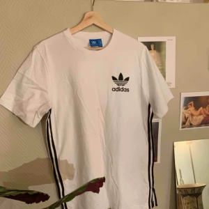  - Adidas T-shirt med svarta ränder på sidorna, aldrig använd. (Fraktkostnaden står köparen för)
