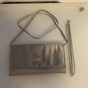  - Bal/sittningsväska. Funkar som clutch eller med ett av två möjliga band. Det ena (metallbandet) finns i en lite kortare och en lite längre längd ☺️