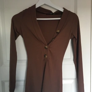  - En brun, v-ringad, ribbad top med fyra knappar. Helt oanvänd och etiketten är fortfarande kvar. Säljer pga att den var för v-ringad för min smak. Köparen står för frakt.