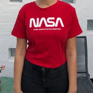 Söt topp med NASA print stl s - Röd t-shirt som är croppad och med printet ’NASA’ på. Stl. s. Knappt använd. Fungerar även som tröja för barn. Kunden står för fraktkostnaden om du inte vill hämta varan. 