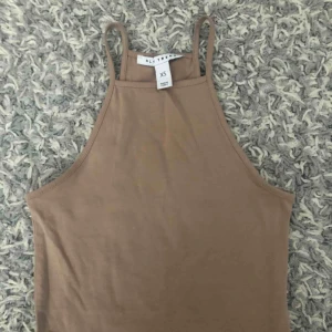  - En halterneck topp i en beige färg som är lite cropped i modellen.