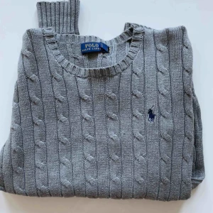  - Kabelstickad Ralph Lauren Polo i nyskick. Som ni ser är det inga nopprar eller sånt som uppkommit efter användning då den är oanvänd. Mörkgrå och jättemysig, köpt för ca 1000 kronor, 