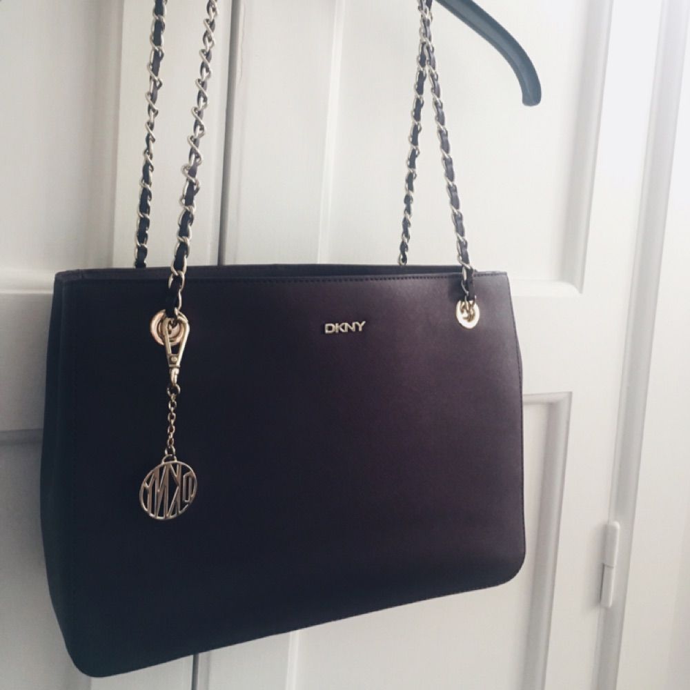 Äkta DKNY Purple Saffiano Burgundy Medium Tote Bag. Jättesvår färg att fånga på bild men den är mörklila, på sista bilden ser den nästan svart ut pga ljuset, men ville bara visa att den är i bra skick! Använd fåtal gånger, inga revor eller märken på väskan! Flera fack inuti och DKNY mönstrat foder. Gulddetaljer på kedjan och hänget vilket knappt syns men skickar jättegärna fler bilder vid förfrågan! Säljer pga inte riktigt min stil längre, nypris €236 men är villig att diskutera pris! Köpare står för eventuell frakt . Väskor.