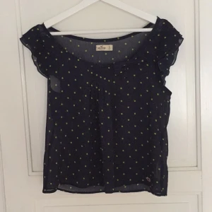  - Super söt marinblå blus med gröna prickar och en rosett på sidan av urringningen. Blusen är kommer ifrån Hollister och är i storleken small.