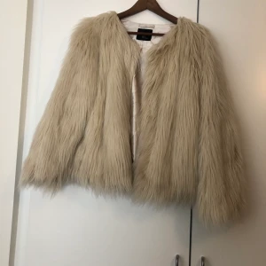 Jacka med fejkpäls - Jättefin jacka i beige fejkpäls. I använt men fint skick. Storlek M. Hämtas i Bro eller skickas med post (fraktkostnad tillkommer). 